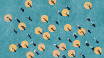 Photo looking down on a stylised background in teal blue with a set of overlapping hexagon outlined and yellow circles. These have a range of people standing in the circles or elsewhere with their shadows falling to the lower right.